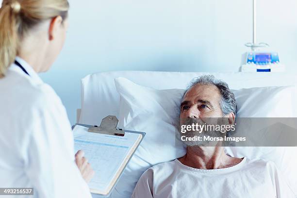 doctor writing notes while talking to male patient - hospital bed stock pictures, royalty-free photos & images