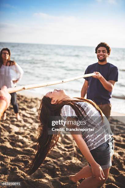 friends playing limbo on the beach - limbo stockfoto's en -beelden