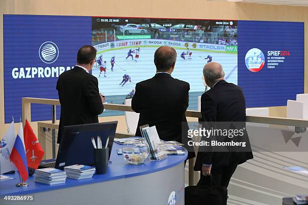 Businessmen pause to watch ice hockey on a digital screen at the OAO Gazprom pavilion at the St. Petersburg International Economic Forum in Saint...
