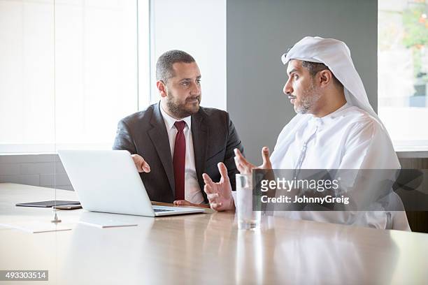 two middle eastern businessmen in meeting using laptop - business man stock pictures, royalty-free photos & images