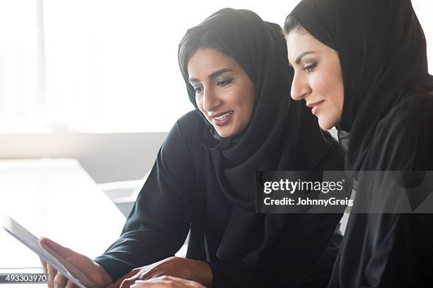 two middle eastern businesswomen wearing hijabs using tablet - emirati at work stock pictures, royalty-free photos & images