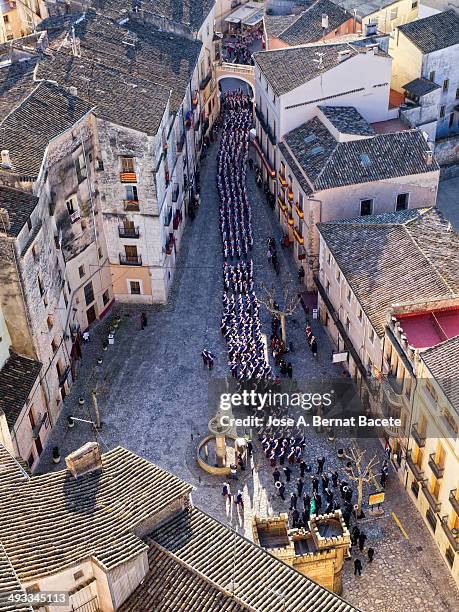 Village square at parties "Moros y Cristianos" in it are a group of people marching in traditional costumes.