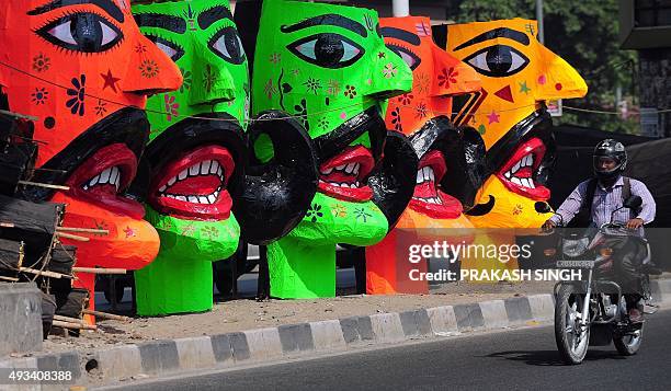 An Indian motorcyclist passes by the effigies of the demon king of Hindu Mythology, Ravana, displayed for sale at a roadside in New Delhi on October...