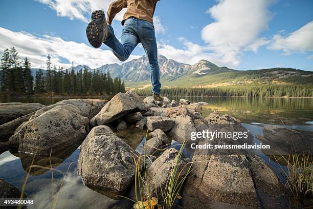 hiker jumps rock to rock in mountain lake - jasper national park stock pictures, royalty-free photos & images