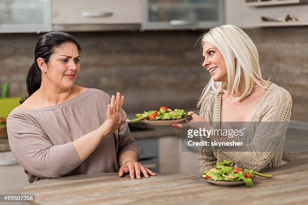 fat woman refusing healthy salad form her friend. - weigeren stockfoto's en -beelden