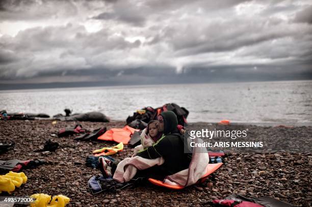 Man sits with a young girl wrapped in a blanket on the shore after arriving with other refugees and migrants on the Greek island of Lesbos after...