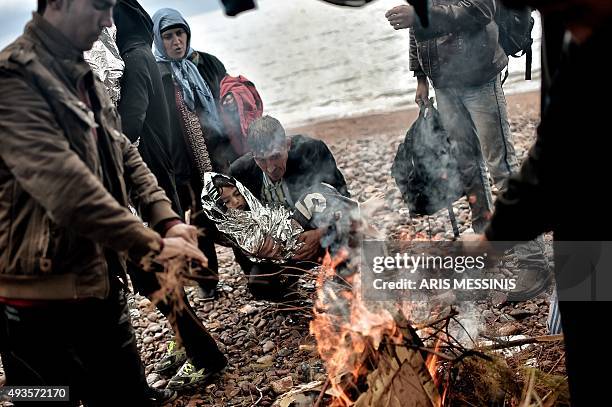 Man holds a child wrapped in an emergency blanket as refugees and migrants warm themselves near a fire after arriving on the Greek island of Lesbos...