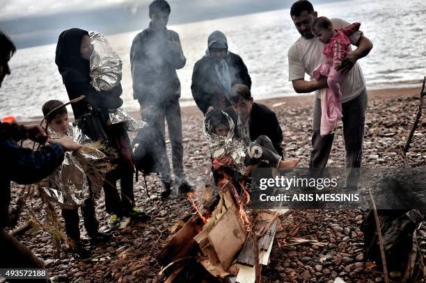 Man holds a child wrapped in an emergency blanket as refugees and migrants warm themselves near a fire after arriving on the Greek island of Lesbos...