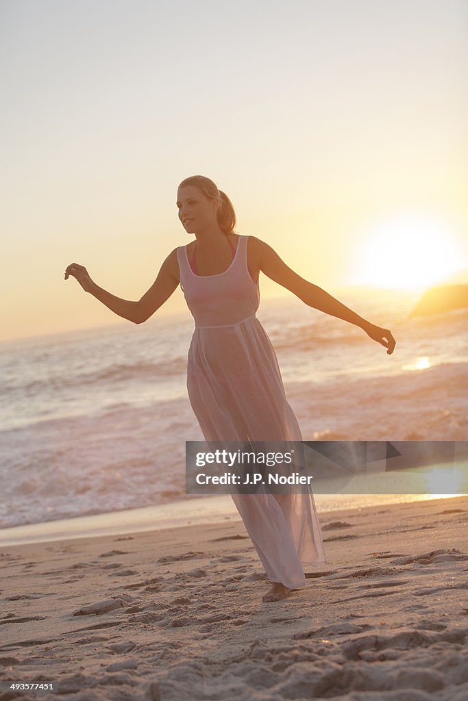 Young woman in white dress on the beach at sunset