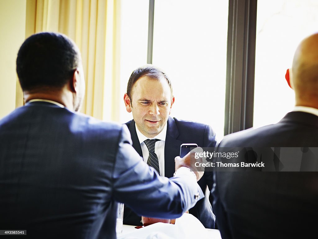 Businessman showing smart phone to colleague