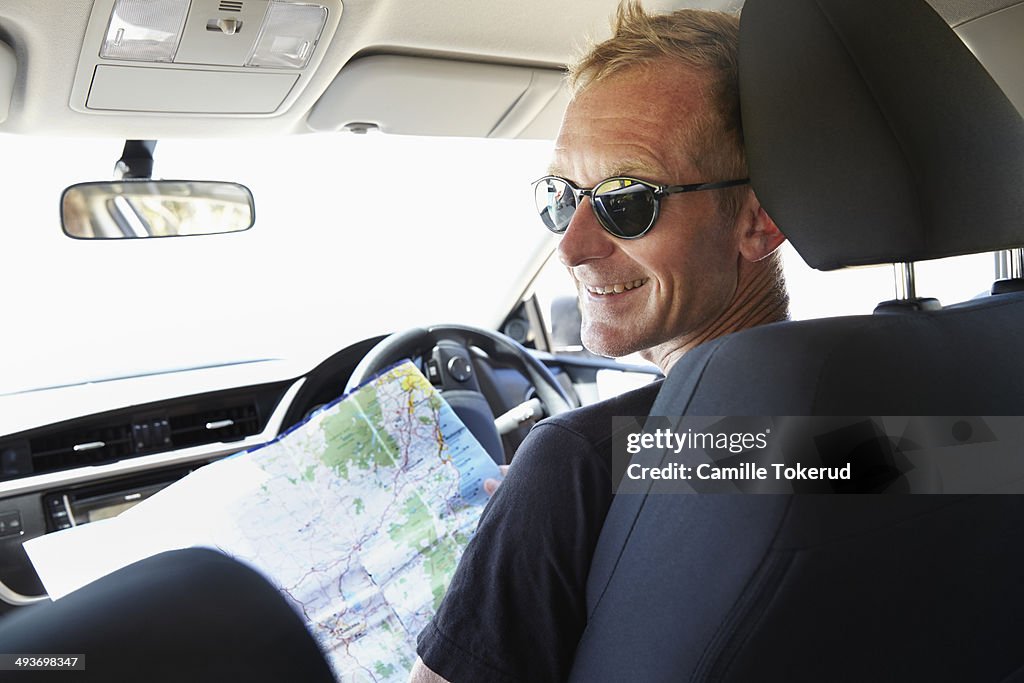 Man holding map inside a car smiling