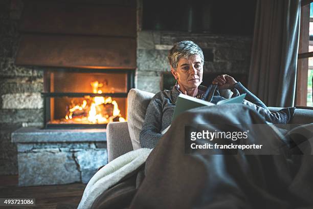 woman reading a book on the couch - haardvuur stockfoto's en -beelden