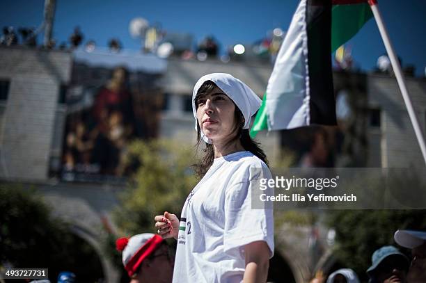 People wait in Manger Square for Pope Francis to take part in a Mass held at the Church of Nativity as crowds watch and wave flags in the foreground...