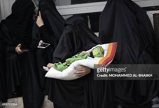 Bahraini Shiite Muslim woman carries a baby during a ceremony commemorating Ashura, which marks the seventh century slaying of Imam Hussein, the...