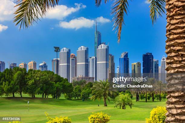 dubaï, émirats arabes unis-parcours de golf de premier plan et les gratte-ciel en toile de fond - green de golf photos et images de collection