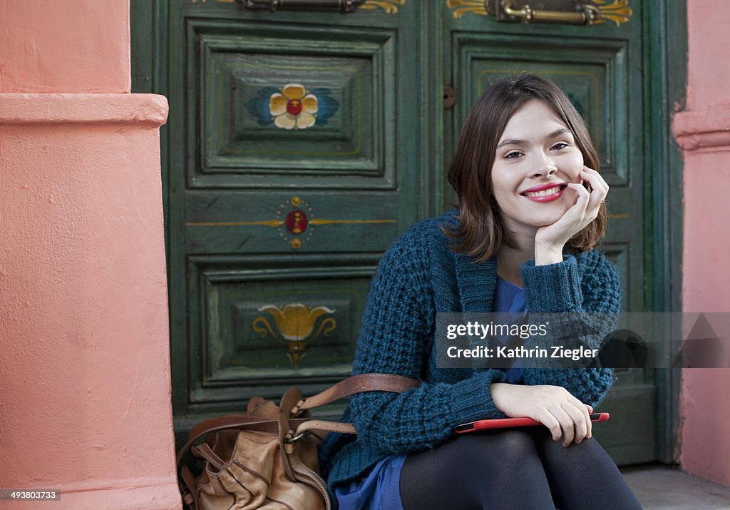 Young woman sitting on doorstep, smiling
