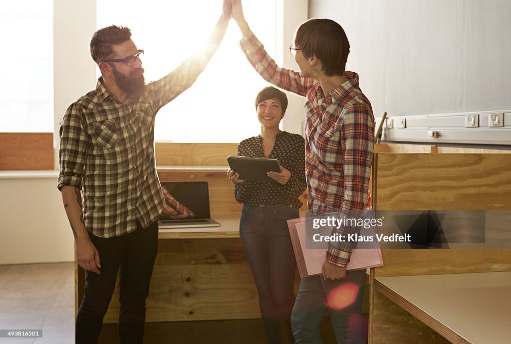 Creative coworkers doing high five at office