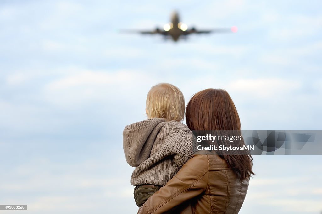 Woman holding toddler with airplane on background