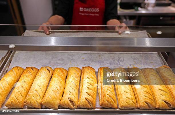 An employee holds a tray of freshly baked sausage rolls in a Greggs Plc sandwich chain outlet in Caterham, U.K., on Thursday, Oct. 22, 2015....