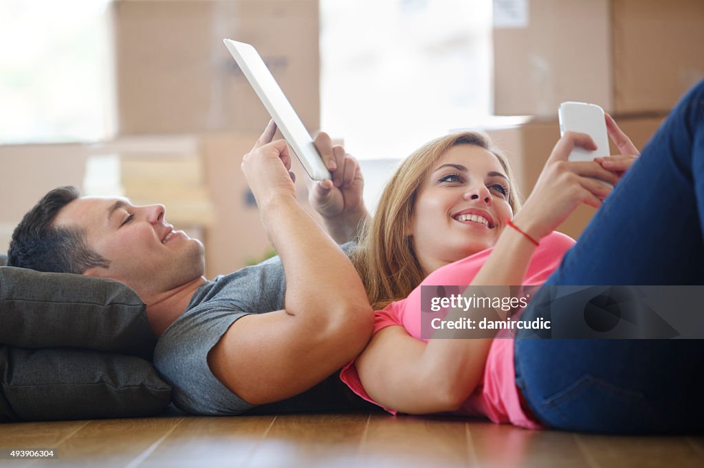 Young couple using mobile phone and tablet in new home