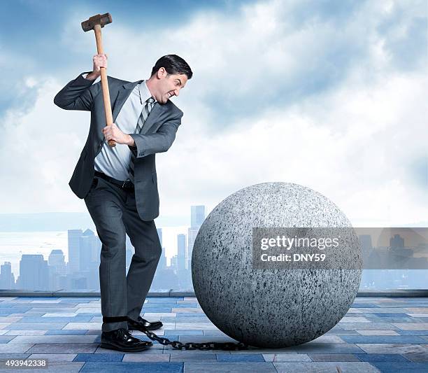 businessman using sledgehammer to break free of ball and chain - sledgehammer stockfoto's en -beelden