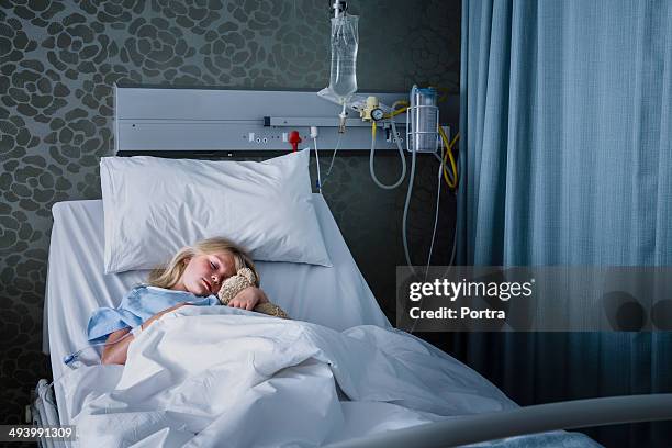 little girl and a teddy bear in a hospital bed. - child hospital stock pictures, royalty-free photos & images