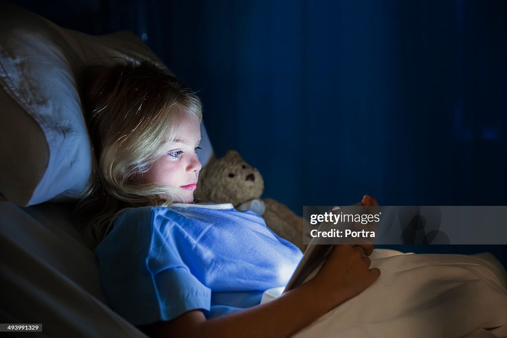 Girl in hospital bed using digital tablet.