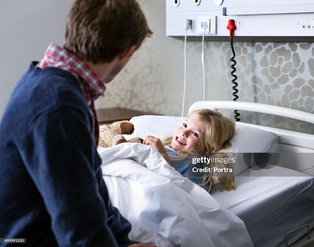 Happy girl in a hospital bed talking to her dad.