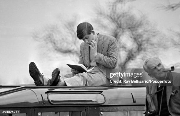 Prince Charles sitting atop a car and looking at a book during the Badminton Horse Trials in Gloucestershire on 9th April 1965.