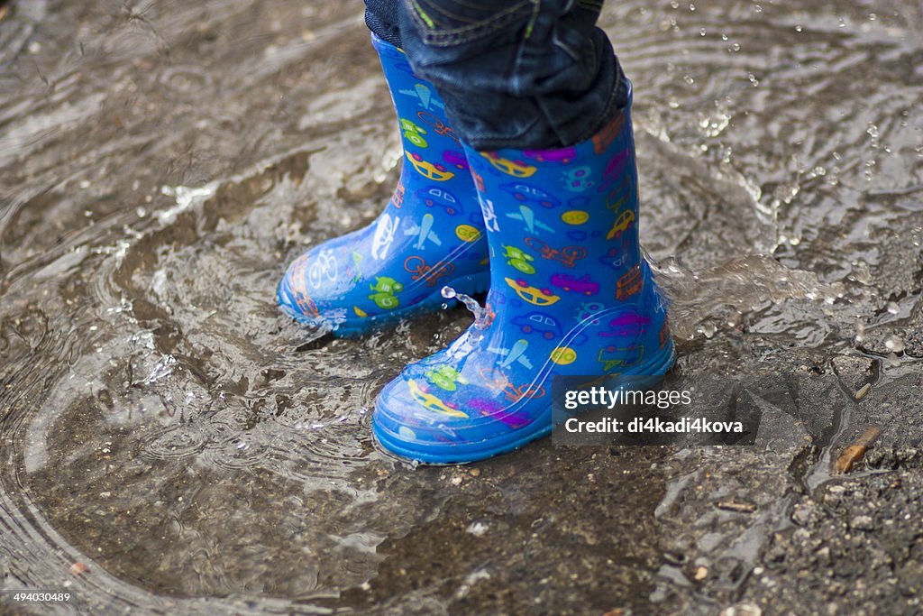 Boy with blue rubber boots in puddle