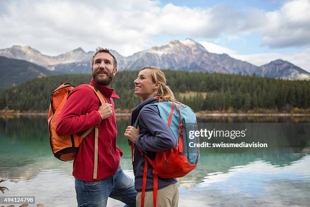 young cheerful couple hiking by the lake in autumn - backpacker travel stock pictures, royalty-free photos & images