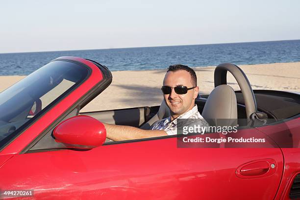 young man cruising in a convertible along a beach - man driving sports car stock pictures, royalty-free photos & images