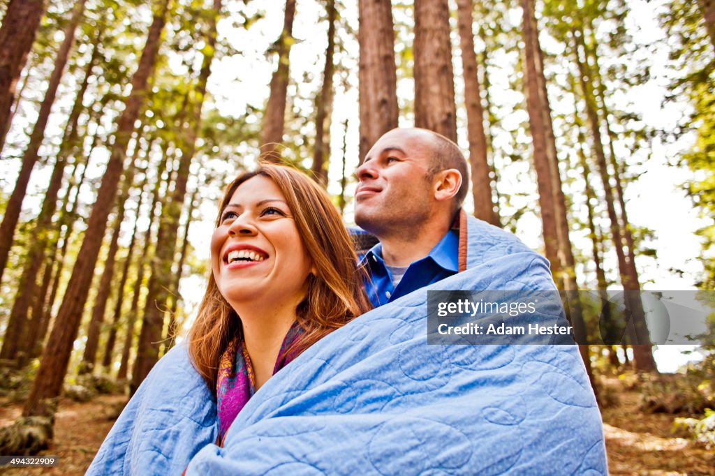 Hispanic couple wrapped in blanket in forest