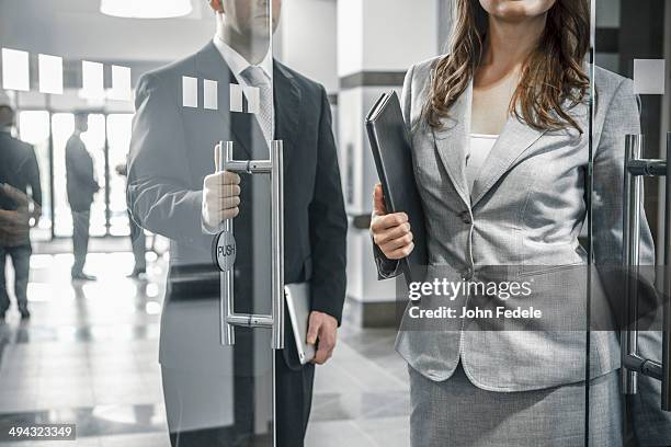 businessman holding door open for female colleague - etiquette stock-fotos und bilder