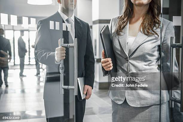 businessman holding door open for female colleague - social grace stock pictures, royalty-free photos & images
