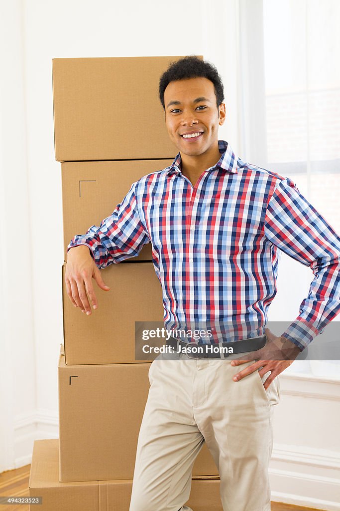 Mixed race man standing by cardboard boxes in new home