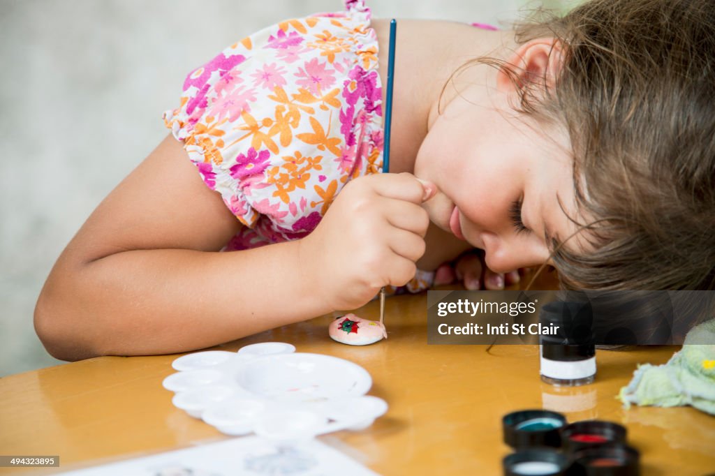 Caucasian girl painting rock on desk