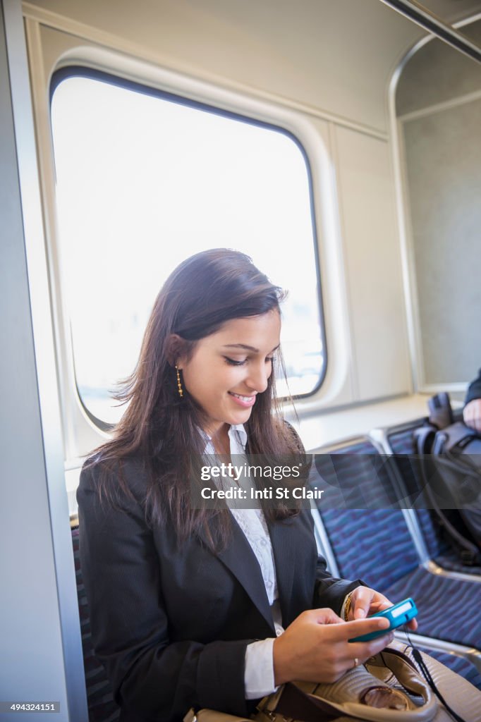 Mixed race businesswoman using cell phone on train