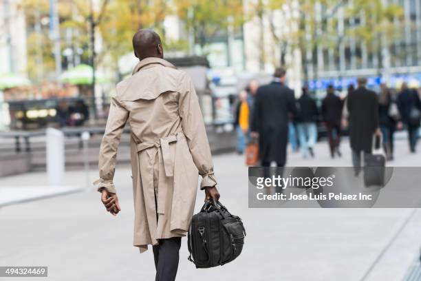 black businessman carrying bag on city street - trench coat stock pictures, royalty-free photos & images
