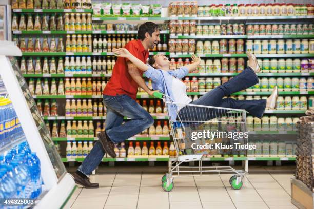 caucasian couple playing in grocery store - man pushing cart fun play stock pictures, royalty-free photos & images