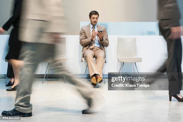 businessman using cell phone in busy lobby area - busy lobby stock pictures, royalty-free photos & images