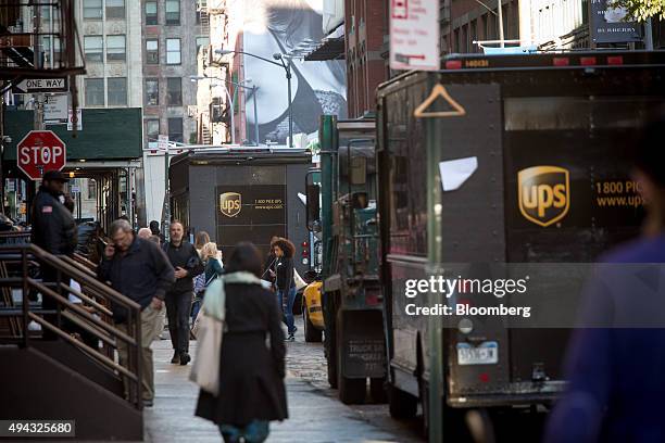 Pedestrians walk past parked United Parcel Service Inc. Trucks in New York, U.S., on Friday, Oct. 23, 2015. UPS is scheduled to release third-quarter...