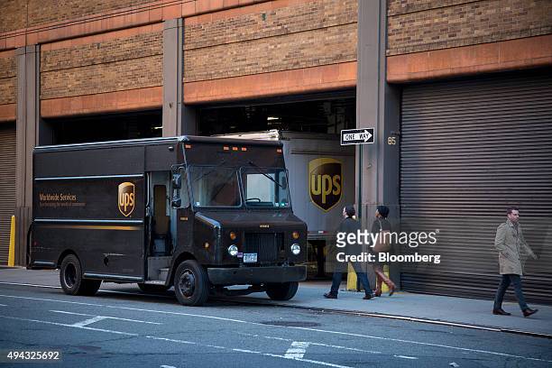 Pedestrians walk past trucks parked at a United Parcel Service Inc. Facility in New York, U.S., on Friday, Oct. 23, 2015. UPS is scheduled to release...