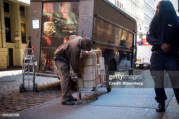 United Parcel Service Inc. Driver, center, loads a cart with boxes as a FedEx Corp. Driver, right, watches in New York, U.S., on Friday, Oct. 23,...