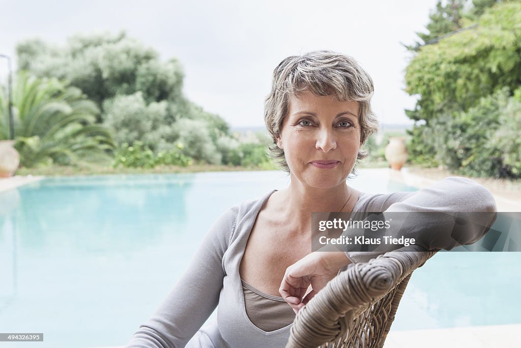 Woman smiling in armchair by swimming pool