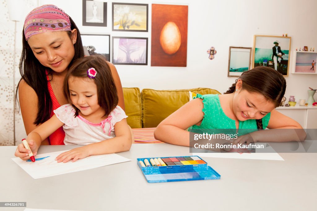 Mixed race mother and daughters coloring in kitchen