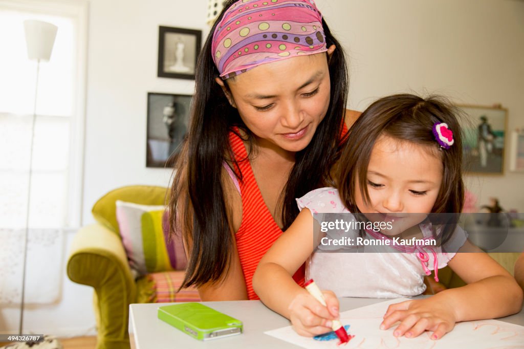 Mixed race mother and daughter coloring in kitchen