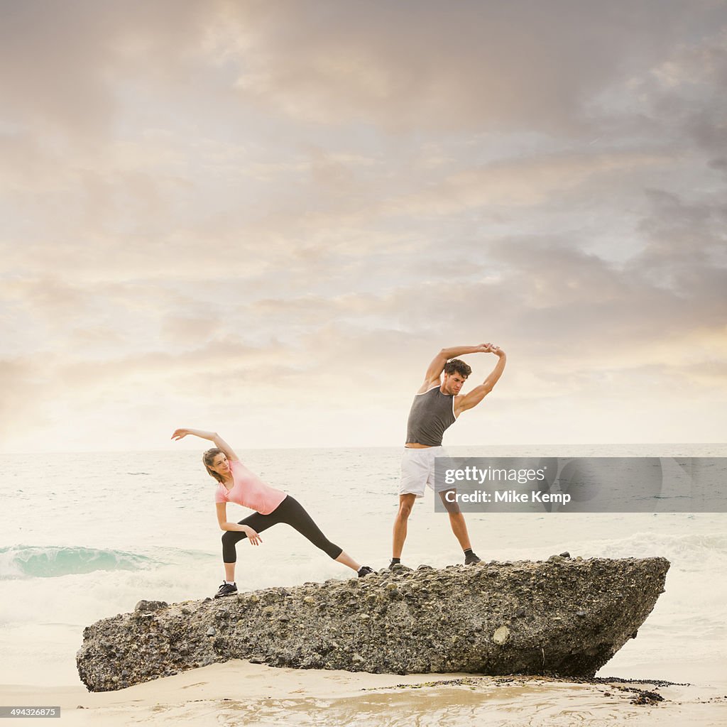 Caucasian runners stretching on beach