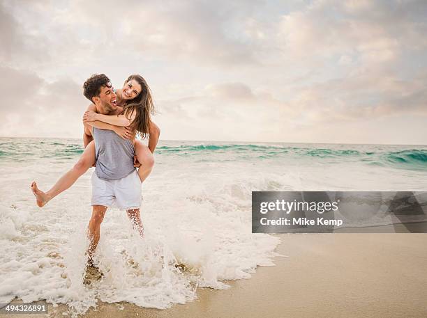 caucasian couple playing on beach - huckepack nehmen stock-fotos und bilder