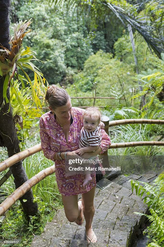 Caucasian mother carrying baby up steps in jungle landscape